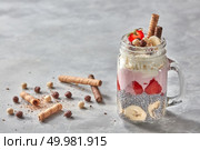 Mason Jar Bank with a layered dessert of yoghurt, strawberry, banana and chia pudding, decorated with biscuits and whipped cream on concrete background. Mason jar with yogurt, berries and chia pudding on concrete background with cookies. Стоковое фото, агентство Ingram Publishing / Фотобанк Лори