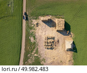The field with bales of straw into the stack after harvesting the grain. Top view. Natural ecological fuel and fertilizers for agricultural work.. Aerial view from drone into area with stacks of straw after harvesting the grain and dirty road with tractor on it. Стоковое фото, агентство Ingram Publishing / Фотобанк Лори