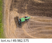 Birds eye view from the drone of the field after harvest. The tractor plows the field, preparing the soil for agricultural work. Top view. Top view of green tractor plowing the ground after harvesting on the field in the autumn time. Top view. Стоковое фото, агентство Ingram Publishing / Фотобанк Лори