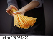 outstretched female hand a handful of raw long thin spaghetti pasta on a dark background. Mediterranean healthy diet. Hands holding raw homemade yellow pasta in dark background. Стоковое фото, агентство Ingram Publishing / Фотобанк Лори