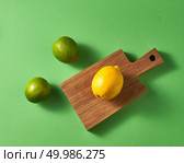 Natural organic citrus fruits on a green background. Top view of a group of green limes and one yellow lemon on a wooden cutting board.. Ripe bright green limes and one yellow lemon on a wooden board on a green background. Top view. Стоковое фото, агентство Ingram Publishing / Фотобанк Лори
