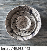 Set of porcelain handcraft plates or bowls, one inside the other on a gray wooden table. Traditional ceramic vintage handmade dishes. Top view. Clay handcraft empty gray bowls, covered with glazed a gray wooden background with copy space. Flat lay. Стоковое фото, агентство Ingram Publishing / Фотобанк Лори