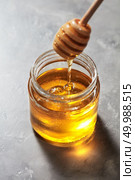 Dripping sweet natural organic honey from stick into glass jar on a gray marble background, pure natural raw sweet goodness.. Natural sweet golden dripping honey in a glass pot with dipper on a gray stone table. Rosh hashanah jewish holiday. Стоковое фото, агентство Ingram Publishing / Фотобанк Лори