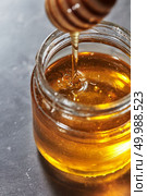 Dripping sweet honey into a glass pot of fresh organic syrup on a gray background. Jewish New Year healthy holiday concept. Traditional useful sweetness.. Organic sweet flower hohey dripping from stick into glass pot on a gray table. Rosh hashanah jewish New Year holiday. Стоковое фото, агентство Ingram Publishing / Фотобанк Лори