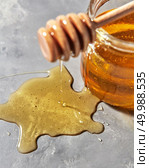 Dripping organic natural fresh honey from wooden stick on a gray kitchen background. place under text. Rosh hashanah jewish New Year holiday concept.. A puddle of a natural floral sweet dessert and dripping honey from wooden honey dipper on a gray stone table. Стоковое фото, агентство Ingram Publishing / Фотобанк Лори