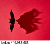 Black handmade craft paper bat with shadow on red background and copy space. Creative mystical halloween card. Flat lay. Mystical card made of hand craft paper bat with a pattern from a shadow on a red background with copy space for text. Halloween. Flat lay. Стоковое фото, агентство Ingram Publishing / Фотобанк Лори