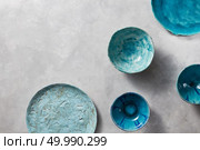 Clay handcraft empty blue plates, bowls, covered with glazed, place text on a gray concrete surface with space for text. Flat lay. Porcelain blue bowls and plates on a gray marble table. Multi-colored ceramic vintage handmade dishes. Стоковое фото, агентство Ingram Publishing / Фотобанк Лори