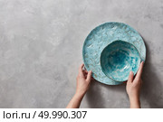 Colorful porceain vintage handmade dishes on a gray marble table with copyspace. Woman hands take ceramic bowl. Top view.. Vintage painted glazed plates dishes on gray concrete table with free space ror text. Girl hold handcraft bowl in her hand. . Стоковое фото, агентство Ingram Publishing / Фотобанк Лори