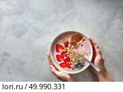 Light greek yogurt or cream dessert with almond flakes, oatmeal and fresh berry served in bowl in female hands on a concrete background, top view with space for text. Cleansing, diet, healthy food, fitness concept.. yoghurt with almond flakes, oatmeal and fresh berry served in bowl in female hands on a concrete background. Стоковое фото, агентство Ingram Publishing / Фотобанк Лори