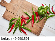 Beautiful composition with a wooden old board and colored hot cayenne peppers and green bell pepper on a white wooden background with space under the text, shot from above. wooden board with colorful peppers and green paprika on a white wooden background. Стоковое фото, агентство Ingram Publishing / Фотобанк Лори