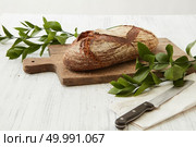 Oval freshly baked bread on a wooden board with a knife and branches of green leaves. Homemade fresh bread. Стоковое фото, агентство Ingram Publishing / Фотобанк Лори