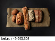 Different kinds of loafs represented on baking paper over black background. Baking and cooking concept background.. Different kinds of bread on background. Стоковое фото, агентство Ingram Publishing / Фотобанк Лори