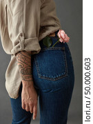 View from the back of a young woman tatoo hand with flower media rose in her pocket. Against a gray background. Mother’s Day,. Young woman with rose media in her pocket. Стоковое фото, агентство Ingram Publishing / Фотобанк Лори