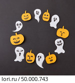 Halloween party handcraft paper card of laughing flying ghosts, spirits, scary pumpkin around it on a black background, place under text. Flat lay. Round frame of handmade horrible smiling spirits and ghosts and laughing pumpkin on a black paper background. Стоковое фото, агентство Ingram Publishing / Фотобанк Лори