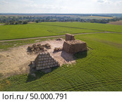 Aerial view from a drone tractor folding a pile of hay in stacks on a green field on a sunny day. Agribusiness concept. Green field with large haystacks and tractor on a sunny day. Aerial view from the drone. Стоковое фото, агентство Ingram Publishing / Фотобанк Лори