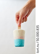 A white blue ice cream on a stick holds a female hand on a gray background with a copy space. Sweet cold dessert. Ice lolly. A girl’s hand holds a homemade sweet ice cream on a gray background with copy space. Summer dessert. Стоковое фото, агентство Ingram Publishing / Фотобанк Лори