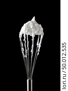 Fresh whipped egg whites on with a metal whisk on a black background with copy space. Cooking concept. A metal whisk with beaten egg whites, represented by a black background with copy space. Ingredient for dessert. Стоковое фото, агентство Ingram Publishing / Фотобанк Лори