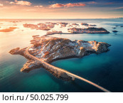 Aerial view of bridge over the sea and mountains in Lofoten Islands, Norway. Henningsvaer at sunset in winter. landscape with azure water, sky with gold sunlight, rocks, buildings, road. Top view. Стоковое фото, агентство Ingram Publishing / Фотобанк Лори