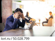 Portrait of Asian Businessman strain and got pressured after see data in smart phone and laptop and fail for his work in cafe with business team in background using for coporate background work. Стоковое фото, агентство Ingram Publishing / Фотобанк Лори