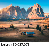 Small wooden houses in beautiful mountain valley at sunset. Autumn landscape with mountains, buildings, hill with yellow grass, trees, high rocks, sky in fall. Alpe di Siusi in Dolomites, Italy. Стоковое фото, агентство Ingram Publishing / Фотобанк Лори