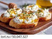 Поджаренный хлеб со взбитым творожным сыром рикотта, медом, зеленью и специями, подается на деревянной доске в качестве полезного утреннего завтрака. Стоковое AI-изображение, AI-художник Катерина Бондарец / Фотобанк Лори