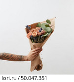 Woman’s hand holds beautiful colourful blossoming flower bouquet of fresh roses living coral color on a light background. Place for text. Mother’s Day.. Delicate flowers living coral roses and eryngium as a beautiful bouquet in girl’s hand with tattoo, copy space. Congratulation card. Стоковое фото, агентство Ingram Publishing / Фотобанк Лори
