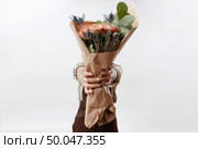 Delicate flowers living coral roses and eryngium as a beautiful bouquet in girl’s hands on a gray background. Place for text. Congratulation card for Woman’s or Mother’s Day.. Lady’s hands hold a nice bouquet from fresh fragrant flowers living coral colored roses on a light background. Copy space. Greeting card for Mother’s Day. Стоковое фото, агентство Ingram Publishing / Фотобанк Лори
