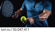 Padel player in action preparing to serve, holding paddle and bright tennis ball, focus on hands and equipment, intense sports moment, dark background. Стоковое AI-изображение, AI-художник Катерина Бондарец / Фотобанк Лори