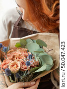 Happy female with ginger hair holds beautiful bouquet of roses living coral colored and eryngium. Gift for Mother’s Day or Woman’s Day. Close up.. Young girl with red hair holds beautiful bunch of roses living coral colored. Close-up. Conept of celebrating of Mother’s Day. Стоковое фото, агентство Ingram Publishing / Фотобанк Лори
