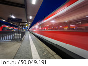 Modern railway station with high speed passenger train on railroad track in motion at night  in Nuremberg, Germany. Fast red commuter train.. Industrial landscape. Стоковое фото, агентство Ingram Publishing / Фотобанк Лори