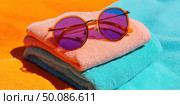 A pair of sunglasses is on top of two towels, one of which is orange. Стоковое AI-изображение, AI-художник Ярославский Максим / Фотобанк Лори