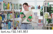 Girl housewife in household store examines package, chooses dishwashing. Стоковое видео, видеограф Яков Филимонов / Фотобанк Лори