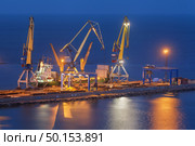 Cargo freight ship with working cranes bridge in sea port at twilight. Sea commercial port at night in Mariupol, Ukraine. Industrial view. Cargo port, logistic. Стоковое фото, агентство Ingram Publishing / Фотобанк Лори