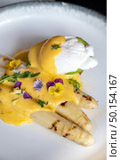 Gourmet grilled white asparagus with poached egg serve with hollandaise savory sauce decorate with edible colorful flowers. Стоковое фото, агентство Ingram Publishing / Фотобанк Лори
