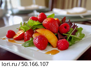 Colorful salad with strawberries and peaches on a bed of mixed greens, beautifully arranged in a white bowl, highlighting fresh ingredients and healthy dining experience. Стоковое AI-изображение, AI-художник Ирина Ручушкина / Фотобанк Лори