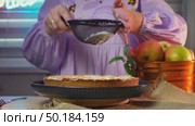 Woman sprinkling flour on homemade apple cake in cozy kitchen setting with fresh fruits. Стоковое видео, видеограф Zakharova Natasha / Фотобанк Лори