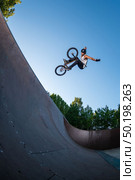 Biker jump high from jump box ramp performing hands off the handlebars trick. Стоковое фото, агентство Ingram Publishing / Фотобанк Лори