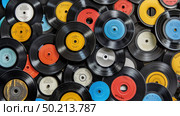 Numerous vintage vinyl records stacked closely side by side in a disorderly pile on a flat surface. Стоковое AI-изображение, AI-художник Данила Большаков / Фотобанк Лори