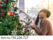 Christmas tree and ornament with background of young Teenager asian couple decorating Christmas tree together prepare for Christmas party holiday. Стоковое фото, агентство Ingram Publishing / Фотобанк Лори