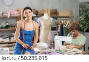 Young female dressmaker inviting clients while man sew. Стоковое фото, фотограф Яков Филимонов / Фотобанк Лори