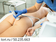 Young woman getting ultrasound cavitation body contouring treatment, anti-cellulite therapy, massage and and moisturizing bottom layer of skin from female cosmetologist. Hardware cosmetology for body sculpting. Стоковое фото, фотограф Яков Филимонов / Фотобанк Лори