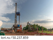 Drilling a well in an oil field. In the foreground is a mobile drilling rig. In the background, oil production at the field using a rocking machine. Summer. Beautiful sky and nature. Стоковое фото, фотограф Владимир Ендовицкий / Фотобанк Лори