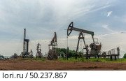 Oil production at the field using two rocking machines. In the background is a drilling rig and equipment for drilling wells. Summer. Beautiful sky and nature. Стоковое фото, фотограф Владимир Ендовицкий / Фотобанк Лори
