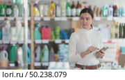 Adult woman looks at the shelves with household chemicals and detergents, she scrolls through the shopping list on phone and looks for the goods she needs in the supermarket. Стоковое видео, видеограф Яков Филимонов / Фотобанк Лори