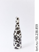 Decorative white painted champagne bottle with black stains on a light grey background, copy space. Minimalism concept.. Creative white wine bottle painted with black spots. Стоковое фото, агентство Ingram Publishing / Фотобанк Лори
