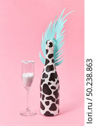 Holiday decorative composition of painted champagne bottle with black spots and paper cut tropical leaf with glass of white powder on a pastel millennial pink background, copy space. Holiday card.. Creative set of painted wine bottle and glass of white powder. Стоковое фото, агентство Ingram Publishing / Фотобанк Лори