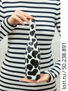 Painted black spots champagne bottle in woman’s hands on striped shirt background, copy space.. Woman dressed in striped shirt holds in hands painted spots wine bottle. Стоковое фото, агентство Ingram Publishing / Фотобанк Лори