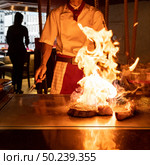 Cooking of beef teppanyaki recipe japanese grilled beef tomahawk steak on cooking pan using scraper with flame in background. Стоковое фото, агентство Ingram Publishing / Фотобанк Лори