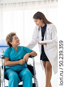 Asian confidence doctor caregiver talking about health concerns with old elderly woman patient sit on wheelchair in hospital ward while daily check up. Стоковое фото, агентство Ingram Publishing / Фотобанк Лори