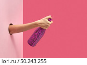 Female’s hand holds painted black spots wine bottle closed by the thumb through the hole in the wall on a duotone pink background with soft shadows, copy space.. The thumb holds closed the wine bottle painted hot pink . Стоковое фото, агентство Ingram Publishing / Фотобанк Лори